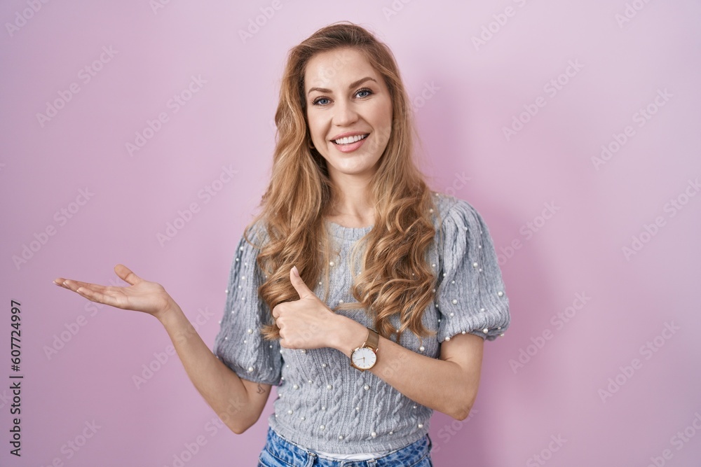 Beautiful blonde woman standing over pink background showing palm hand and doing ok gesture with thumbs up, smiling happy and cheerful Beautiful blonde woman standing over pink background showing palm hand and doing ok gesture with thumbs up, smiling happy and cheerful