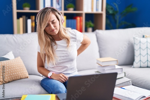 Young blonde woman studying using computer laptop at home suffering of backache, touching back with hand, muscular pain