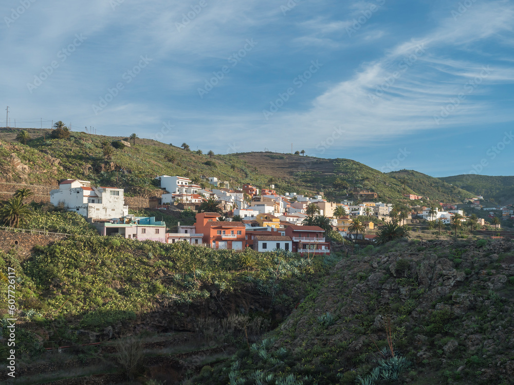 Early morning view of village Arure in green valley with palm trees and traditional colorful houses. Valle Gran Rey, La Gomera, Canary Islands, Spain, Europe. Blue sky white clouds background