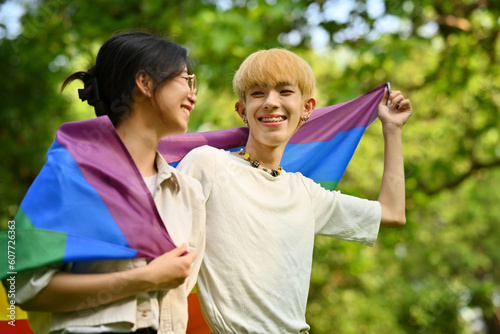 Image of young people with LGBTQ pride flag standing outdoor, supporting LGBTQ community and equality social