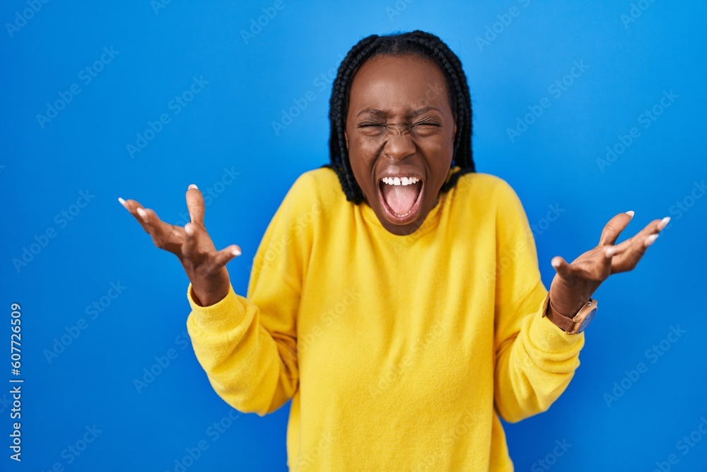 Beautiful black woman standing over blue background celebrating mad and crazy for success with arms raised and closed eyes screaming excited. winner concept Beautiful black woman standing over blue background celebrating mad and crazy for success with arms raised and closed eyes screaming excited. winner concept