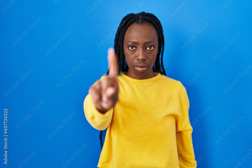 Fototapeta premium Beautiful black woman standing over blue background pointing with finger up and angry expression, showing no gesture