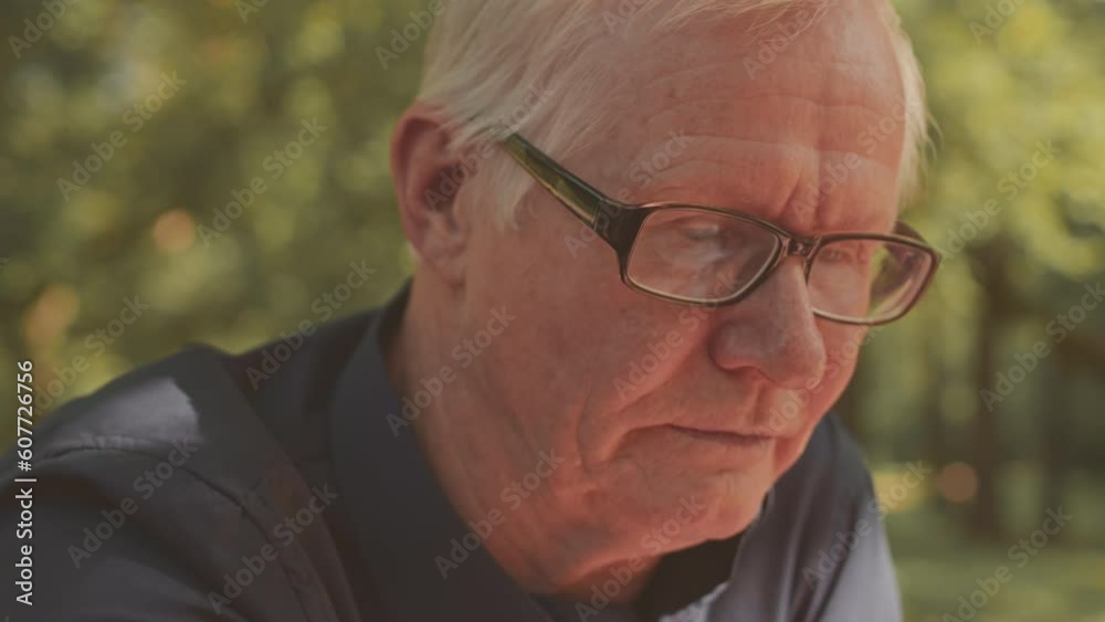 Medium closeup of pensive old Caucasian man in eyeglasses looking at chessboard while thinking of strategy during chess game with opponent outdoors Medium closeup of pensive old Caucasian man in eyeglasses looking at chessboard while thinking of strategy during chess game with opponent outdoors