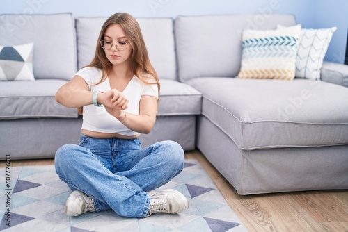 Young caucasian woman sitting on the floor at the living room checking the time on wrist watch, relaxed and confident