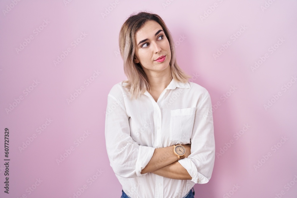 Young beautiful woman standing over pink background looking to the side with arms crossed convinced and confident Young beautiful woman standing over pink background looking to the side with arms crossed convinced and confident