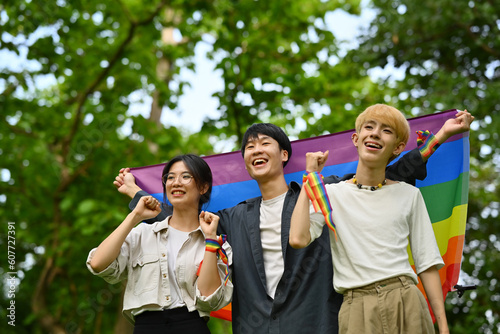 Happy young LGBT friends with rainbow heart celebrating gay pride, enjoying outdoor activities at outdoor