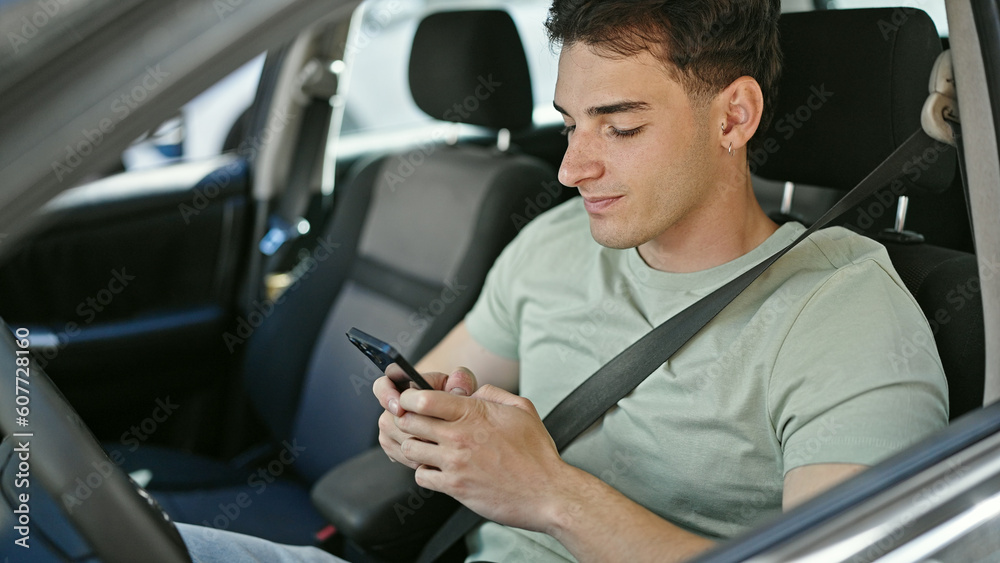 Young hispanic man using smartphone sitting on car at street