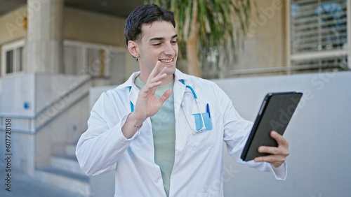 Young hispanic man doctor doing video call with touchpad at hospital