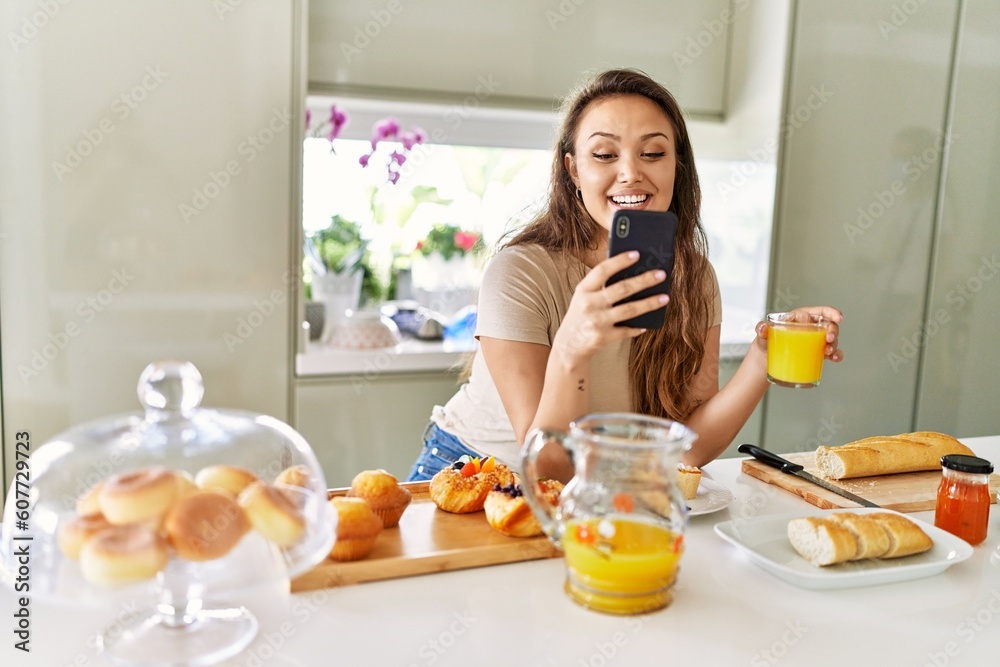 Young beautiful hispanic woman having breakfast using smartphone at the kitchen
