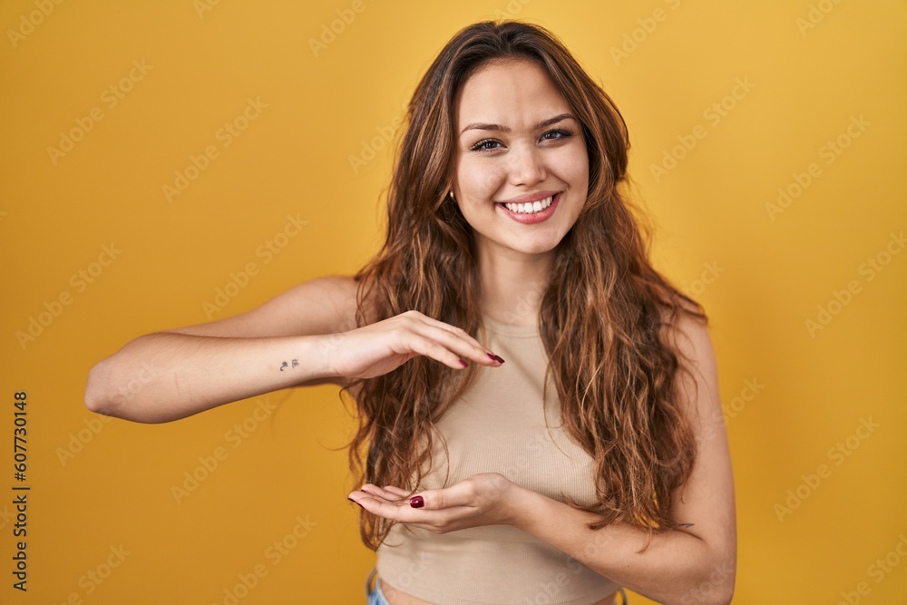 Young hispanic woman standing over yellow background gesturing with hands showing big and large size sign, measure symbol. smiling looking at the camera. measuring concept. Young hispanic woman standing over yellow background gesturing with hands showing big and large size sign, measure symbol. smiling looking at the camera. measuring concept.