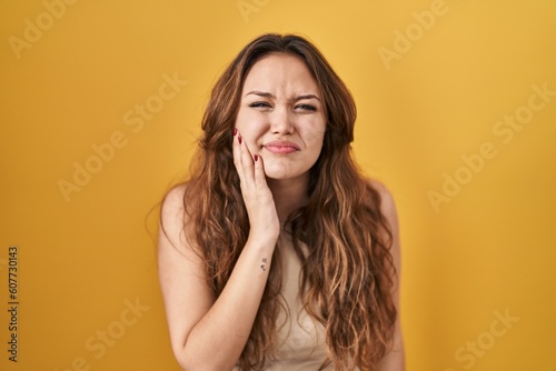 Young hispanic woman standing over yellow background touching mouth with hand with painful expression because of toothache or dental illness on teeth. dentist