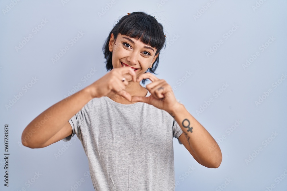 Young hispanic woman wearing casual t shirt over blue background smiling in love doing heart symbol shape with hands. romantic concept. Young hispanic woman wearing casual t shirt over blue background smiling in love doing heart symbol shape with hands. romantic concept.