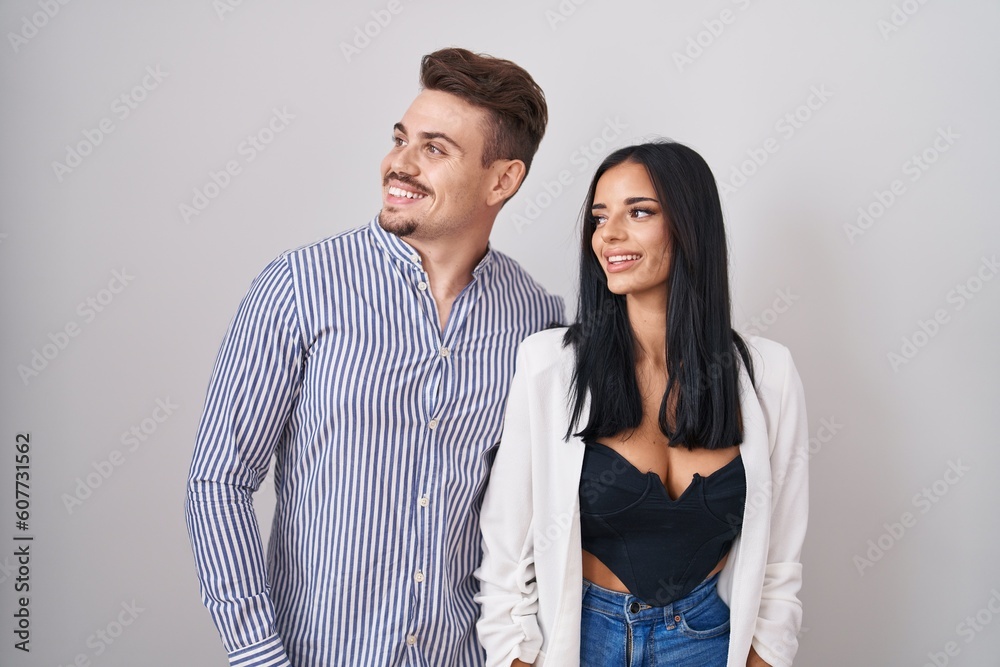 Young hispanic couple standing over white background looking away to side with smile on face, natural expression. laughing confident. Young hispanic couple standing over white background looking away to side with smile on face, natural expression. laughing confident.