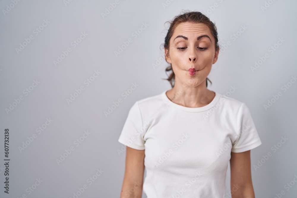 Beautiful brunette woman standing over isolated background making fish face with lips, crazy and comical gesture. funny expression. Beautiful brunette woman standing over isolated background making fish face with lips, crazy and comical gesture. funny expression.