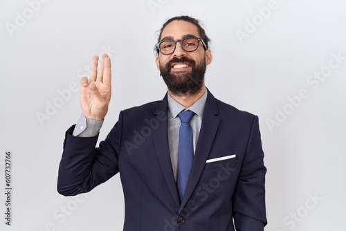 Hispanic man with beard wearing suit and tie showing and pointing up with fingers number three while smiling confident and happy.