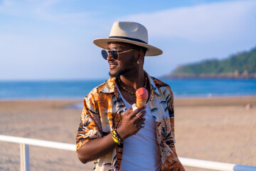 Black ethnic man enjoy summer vacation on the beach eating an ice cream having fun
