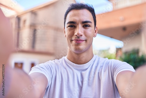 Young hispanic man smiling confident making selfie by camera at street