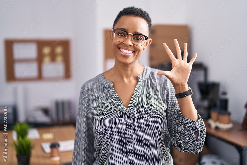 Fototapeta premium African american woman working at the office wearing glasses showing and pointing up with fingers number five while smiling confident and happy.