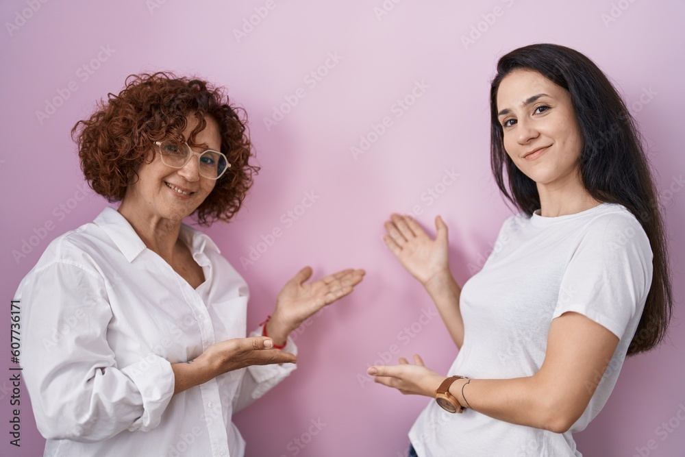 Hispanic mother and daughter wearing casual white t shirt over pink background inviting to enter smiling natural with open hand Hispanic mother and daughter wearing casual white t shirt over pink background inviting to enter smiling natural with open hand