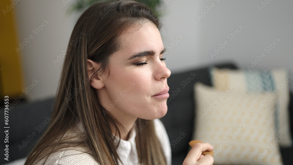 Young beautiful hispanic woman eating cookies sitting on the sofa at home