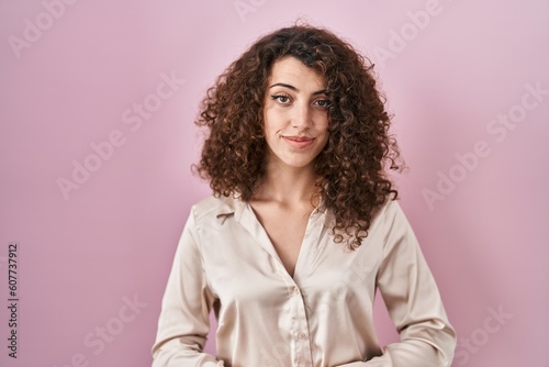 Hispanic woman with curly hair standing over pink background with hands together and crossed fingers smiling relaxed and cheerful. success and optimistic