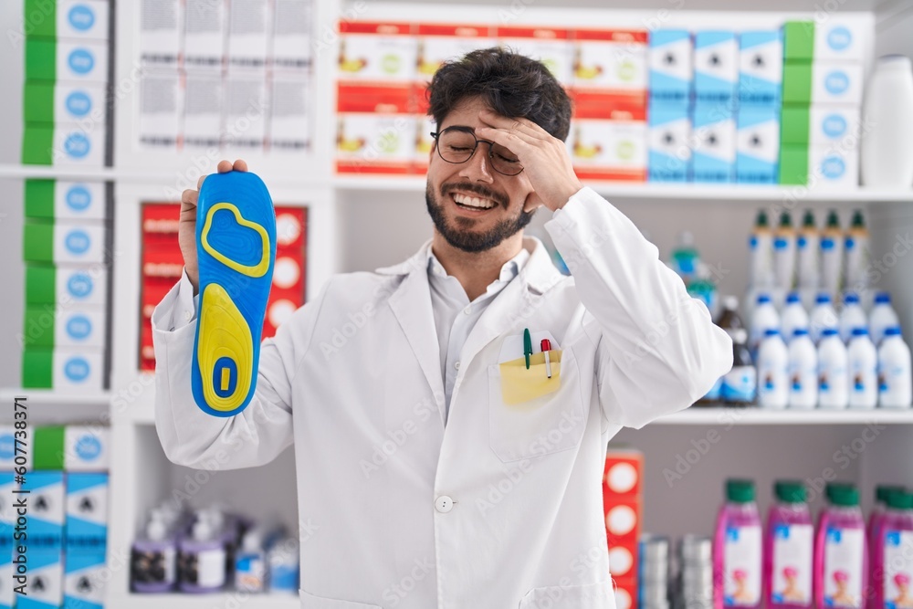 Hispanic man with beard working at pharmacy drugstore holding insole stressed and frustrated with hand on head, surprised and angry face