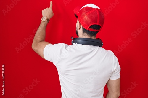 Hispanic man with beard wearing gamer hat and headphones posing backwards pointing ahead with finger hand