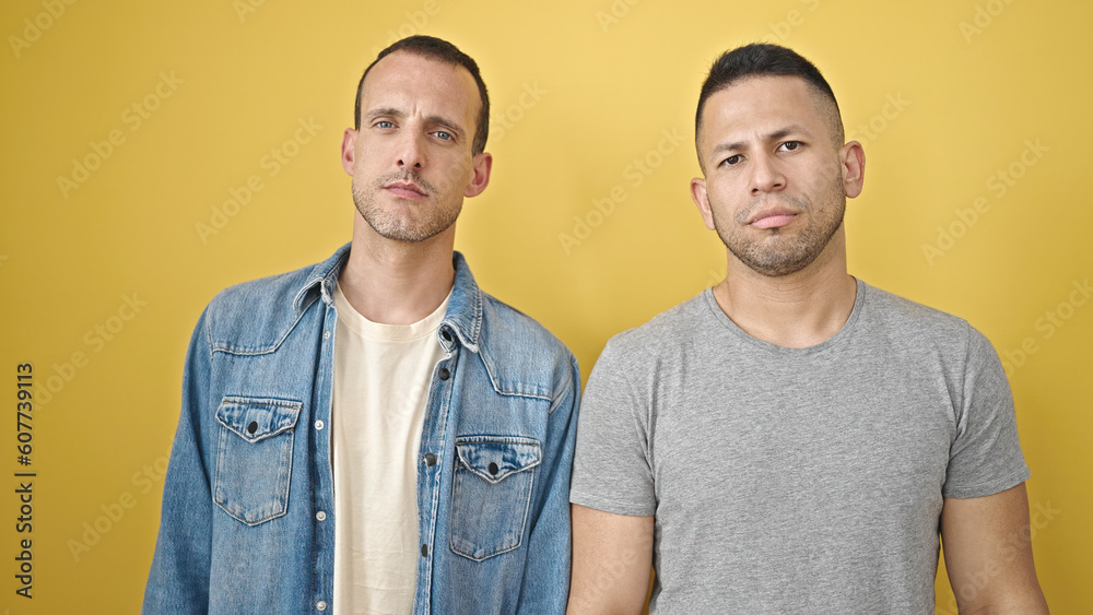 Two men couple standing with relaxed expression over isolated yellow background