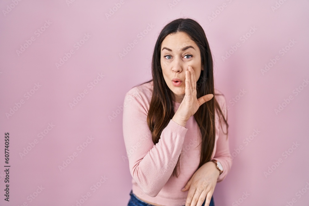 Young brunette woman standing over pink background hand on mouth telling secret rumor, whispering malicious talk conversation Young brunette woman standing over pink background hand on mouth telling secret rumor, whispering malicious talk conversation