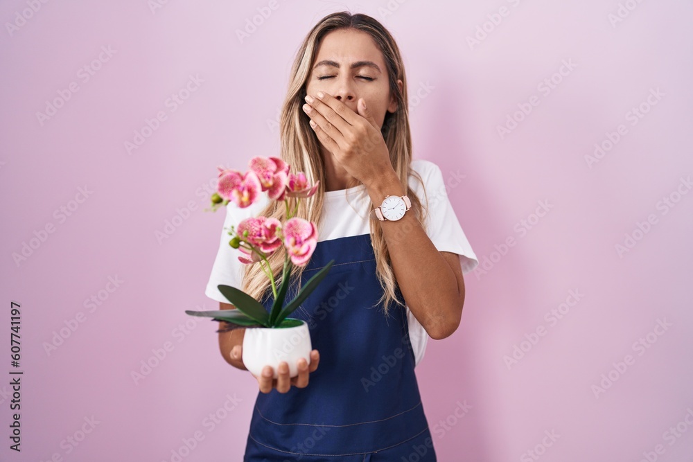 Young blonde woman wearing gardener apron holding plant bored yawning tired covering mouth with hand. restless and sleepiness. Young blonde woman wearing gardener apron holding plant bored yawning tired covering mouth with hand. restless and sleepiness.