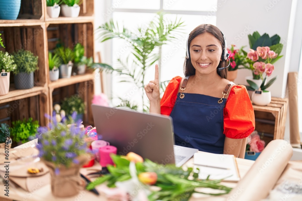 Young hispanic woman working at florist shop doing video call smiling with an idea or question pointing finger with happy face, number one