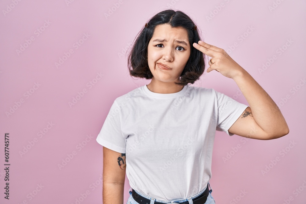 Young hispanic woman wearing casual white t shirt over pink background shooting and killing oneself pointing hand and fingers to head like gun, suicide gesture. Young hispanic woman wearing casual white t shirt over pink background shooting and killing oneself pointing hand and fingers to head like gun, suicide gesture.