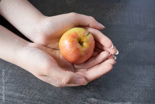 Female hands hold a red apple on a dark wooden background. Close-up.