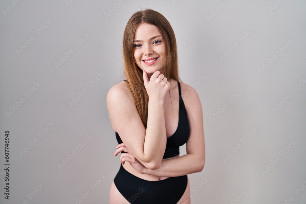 Young caucasian woman wearing lingerie looking confident at the camera smiling with crossed arms and hand raised on chin. thinking positive.