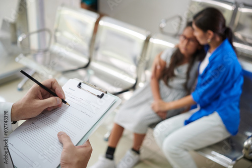 Doctor filling medical card when talking to mother of preteen girl