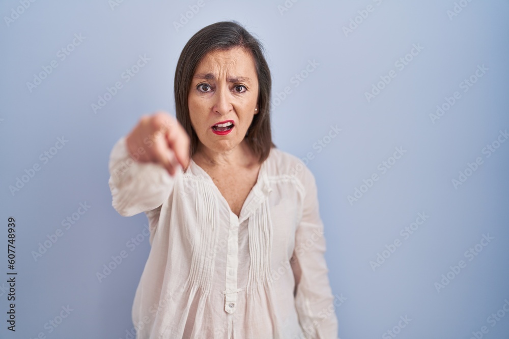 Middle age hispanic woman standing over blue background pointing displeased and frustrated to the camera, angry and furious with you Middle age hispanic woman standing over blue background pointing displeased and frustrated to the camera, angry and furious with you