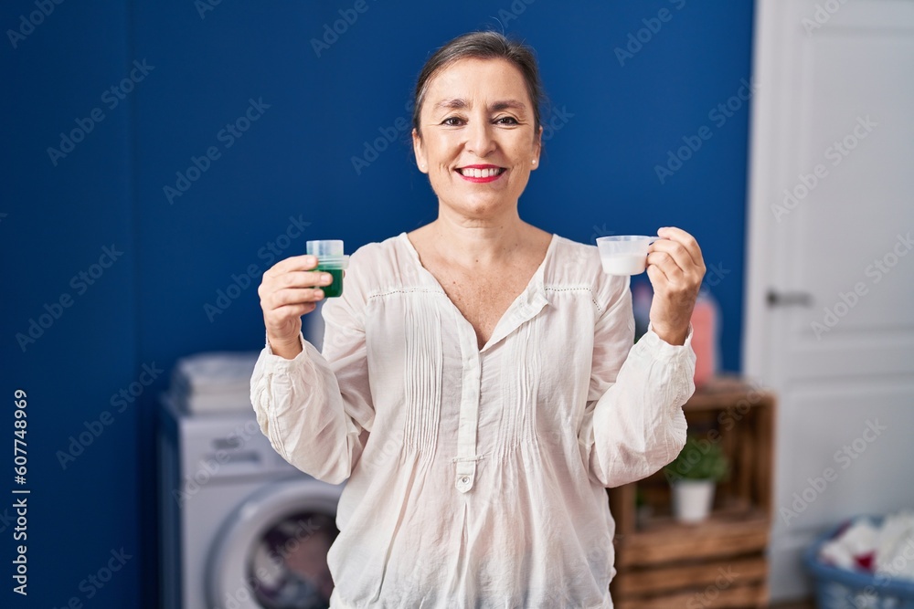 Middle age hispanic woman holding laundry detergent and laundry powder smiling with a happy and cool smile on face. showing teeth. Middle age hispanic woman holding laundry detergent and laundry powder smiling with a happy and cool smile on face. showing teeth.