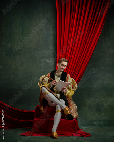 Obraz na plátně Portrait of young male royal person, duke working on tablet against dark green, vintage background
