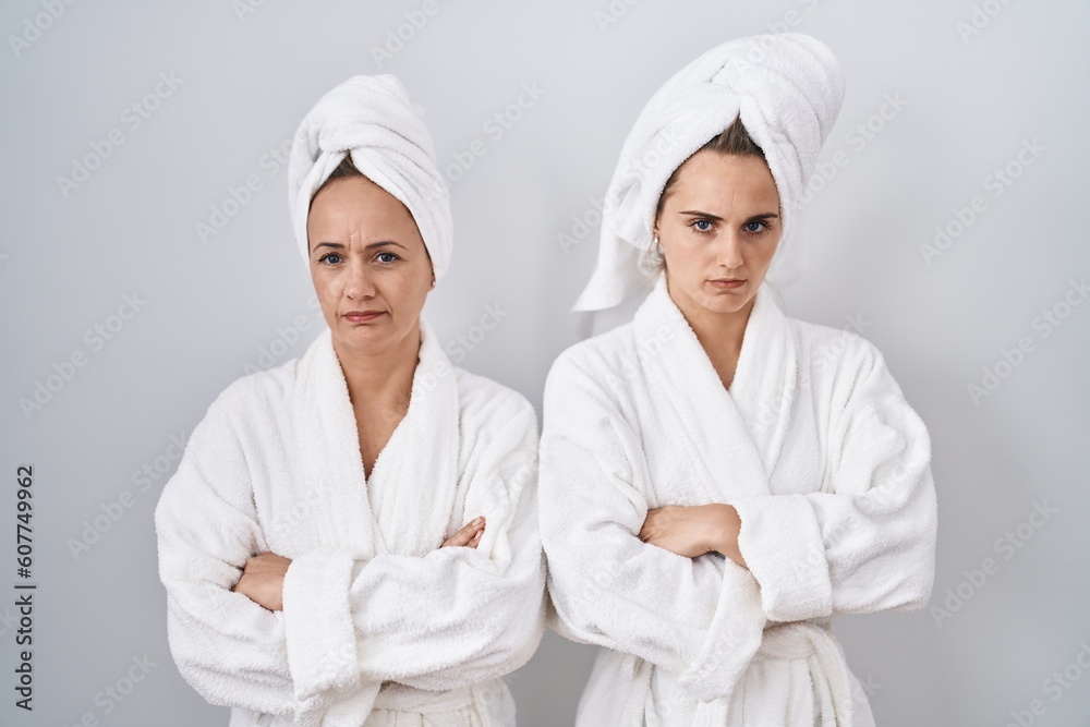 Middle age woman and daughter wearing white bathrobe and towel skeptic and nervous, disapproving expression on face with crossed arms. negative person.