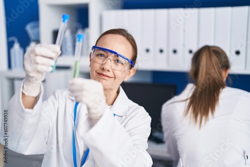 Two women scientists smiling confident holding test tubes at laboratory