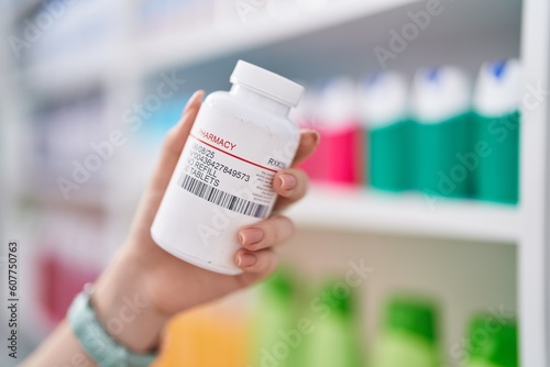 Fototapeta Naklejka Na Ścianę i Meble -  Young caucasian woman holding pills bottle at pharmacy
