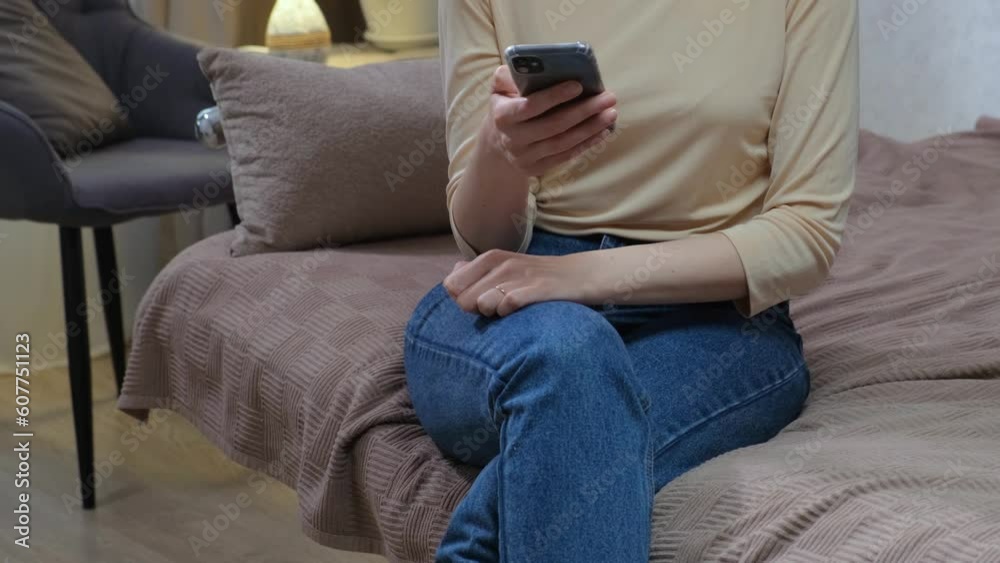 An unrecognizable woman is sitting on the couch with a phone in her hands and using a smartphone in the room. Technology, mobile communication