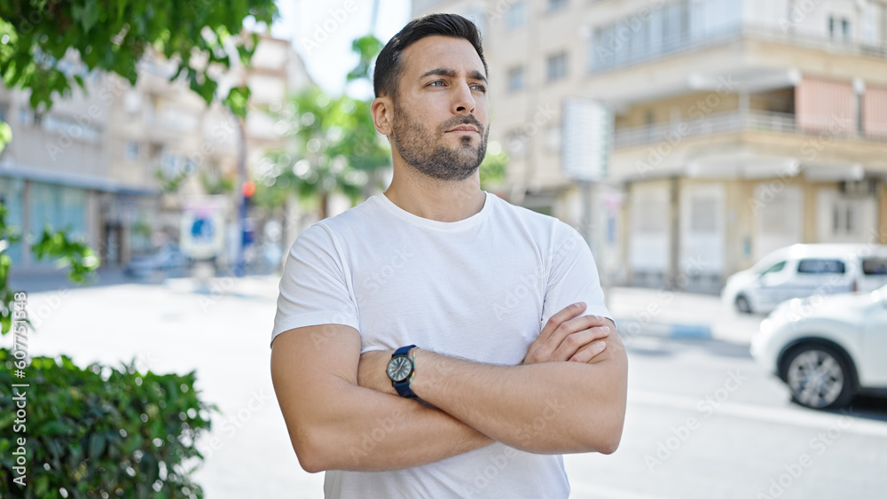 Fototapeta premium Young hispanic man standing with crossed arms and relaxed expression at street