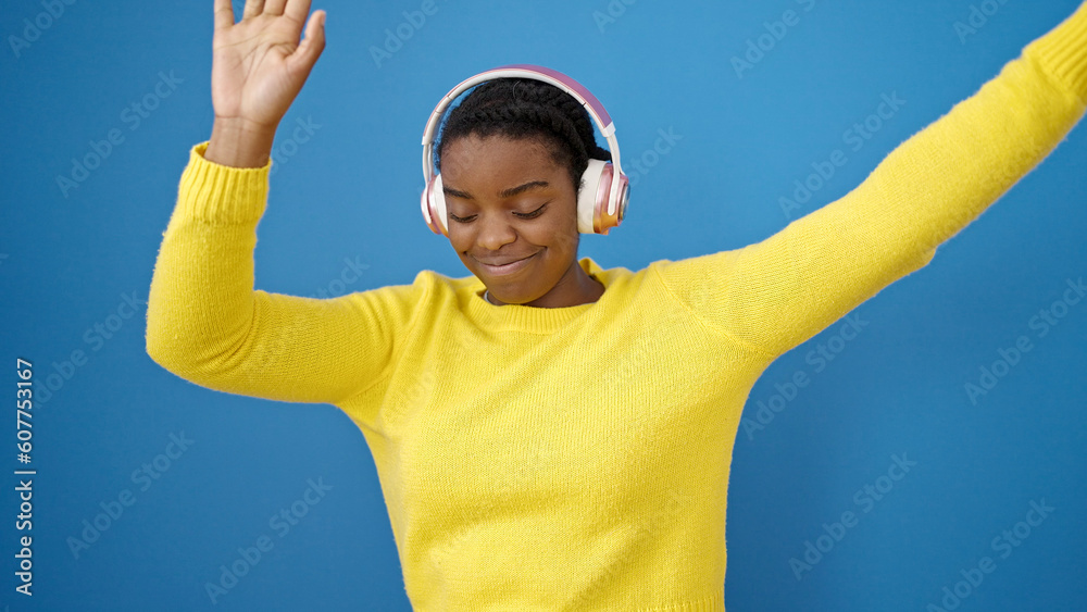 Naklejka premium African american woman dancing wearing headphones over isolated blue background