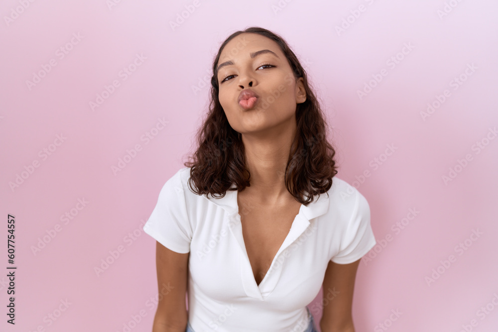 Young hispanic woman wearing casual white t shirt looking at the camera blowing a kiss on air being lovely and sexy. love expression. Young hispanic woman wearing casual white t shirt looking at the camera blowing a kiss on air being lovely and sexy. love expression.