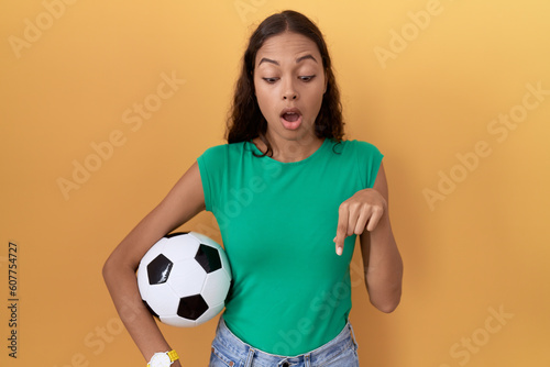 Young hispanic woman holding ball pointing down with fingers showing advertisement, surprised face and open mouth © Krakenimages.com