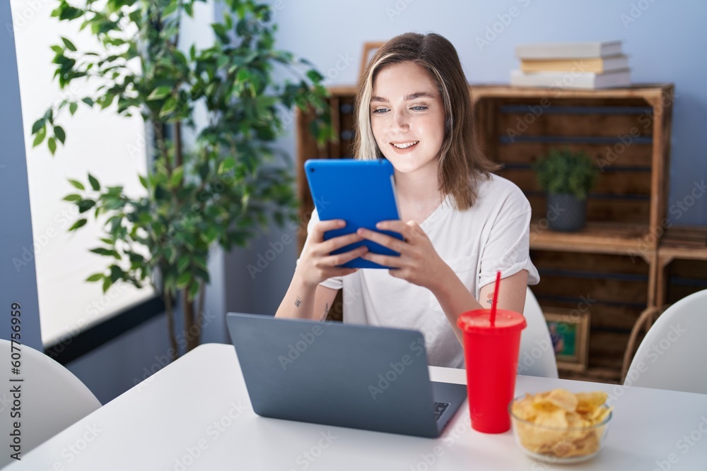 Young woman using touchpad and laptop sitting on table at home Young woman using touchpad and laptop sitting on table at home