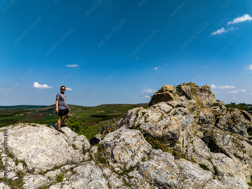 man stands on rocks on top of the hill with blue sky and fields on background