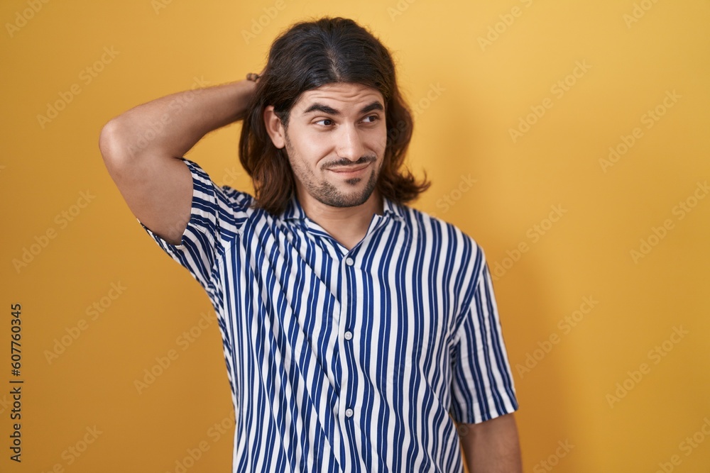 Hispanic man with long hair standing over yellow background confuse and wonder about question. uncertain with doubt, thinking with hand on head. pensive concept. Hispanic man with long hair standing over yellow background confuse and wonder about question. uncertain with doubt, thinking with hand on head. pensive concept.