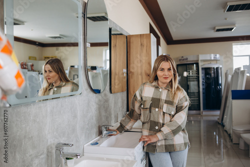 Positive woman customer choosing wash basin in bathroom fitment store photo